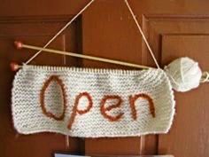 an open sign hanging on a door with yarn and knitting needles in front of it