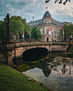 a bridge over a small river in front of a large building with flags on it