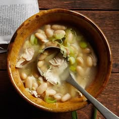 a wooden bowl filled with white bean and meat soup next to a spoon on top of a table