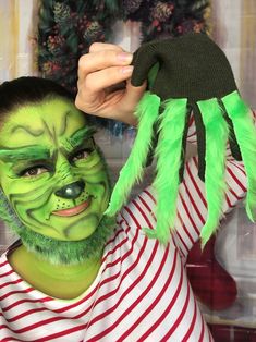 a man with green face paint holding up a fake spider mask on his head and hands