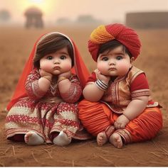 two small children sitting on the ground wearing red and orange outfits with their hands in their mouths