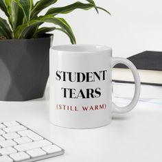 a white coffee mug sitting on top of a desk next to a keyboard and potted plant