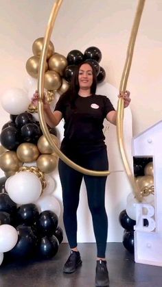 a woman is standing in front of balloons and holding up a large gold hoop with her hands