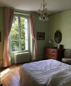 a bedroom with a bed, dresser and chandelier in front of a window