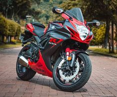 a red and black motorcycle parked on top of a brick road in front of trees