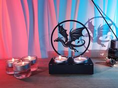 three candles sitting on top of a wooden table next to two glass holders with dragon designs