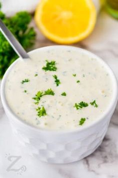 a white bowl filled with broccoli soup next to an orange and parsley