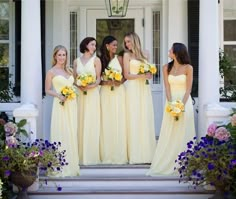 a group of women standing next to each other in front of a white house with yellow and purple flowers