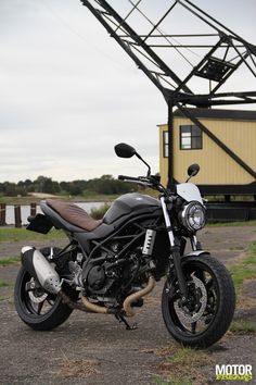 a black motorcycle parked in front of a yellow building with a metal structure behind it