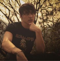 a young man sitting on the ground in front of trees