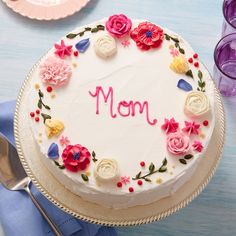 a white cake with flowers and the word mom on it sitting on a blue table