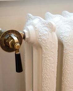 an ornate white radiator with brass knobs on it's side and a black handle