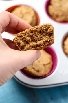 a hand holding a cookie in front of some muffins on a blue surface