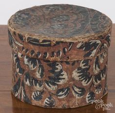 an old wooden box with black and white designs on it sitting on a wood table