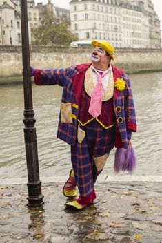 a man dressed as a clown standing next to a lamp post