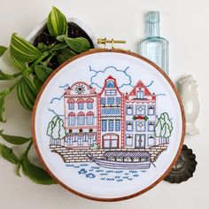 a cross stitch pattern on a wooden hoop with some plants in front of it and a bottle of water next to it