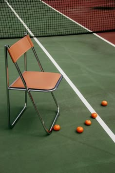 a chair sitting on top of a tennis court with oranges scattered about the ground