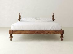 a wooden bed frame with white sheets and pillows on it, in front of a plain wall