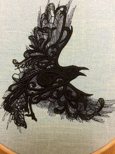 a black bird with feathers on it's back is embroidered onto a piece of fabric