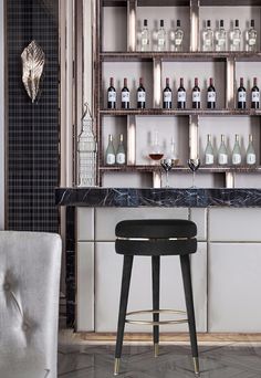 a bar with white stools and bottles on the shelves in front of it, next to a gray chair