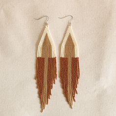 two tone beaded earrings with fringes on white and brown fabric, hanging from hooks