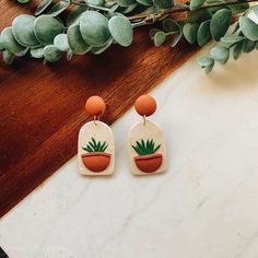 a pair of earrings sitting on top of a wooden table next to a potted plant