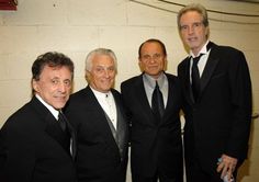 four men in suits and ties standing next to each other with one man wearing a suit