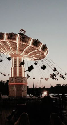 an amusement park ride at dusk with people riding on the swings and flying in the air