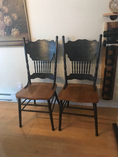 two wooden chairs sitting next to each other on a hard wood floor in front of a wall