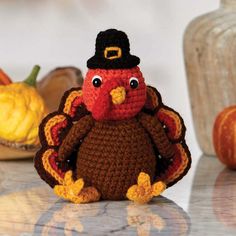 a crocheted turkey sitting on top of a table next to other pumpkins