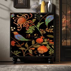 a black cabinet with colorful flowers and birds painted on it's sides, next to framed pictures