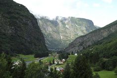 a valley with mountains in the background and houses on the other side, surrounded by trees