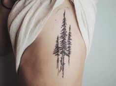 a woman with a tattoo on her back shows the pine trees in the forest behind her