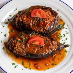 two eggplant stuffed peppers on a white plate with sauce and garnish