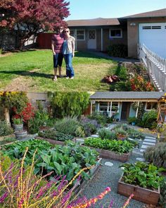 two men standing in front of a garden with lots of flowers and plants around them