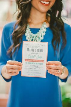 a woman in a blue dress holding up a card with the words bridal shower on it