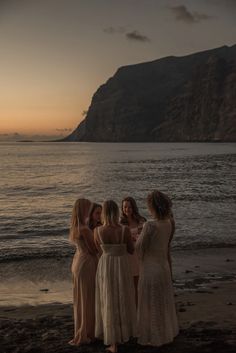 four women standing on the beach at sunset talking to each other, with mountains in the background