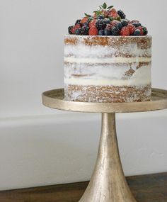 a cake with berries on top sitting on a gold stand in front of a white wall