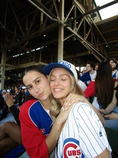 two young women hugging each other in the stands at a baseball game with fans watching