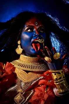 a woman with blue face paint and gold jewelry holding her hand up to her mouth