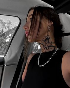 a woman sitting in the back seat of a car with a tattoo on her neck