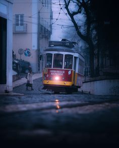 a red and yellow trolley car on street next to building with people walking by it