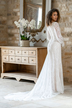 a woman standing in front of a mirror wearing a white wedding dress with long sleeves