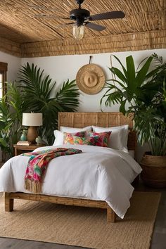 a bed with white sheets and pillows in a bedroom next to potted palm trees