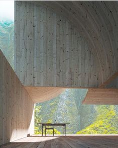 an empty wooden room with a bench in the foreground and mountains in the background