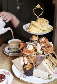 three tiered trays with sandwiches and cakes on them sitting on a wooden table