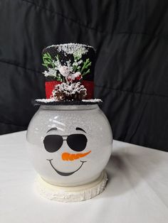 a white vase with a snowman hat and sunglasses on it's head, sitting on a table