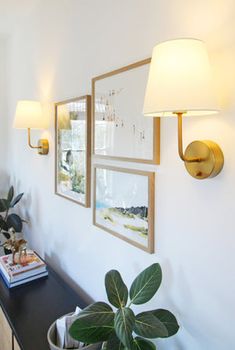 a living room with pictures on the wall and potted plants in front of it