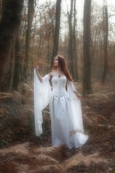 a woman in a white dress is standing in the woods with her arms spread out