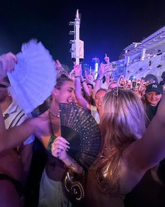 a group of people standing around each other at a music festival with one woman holding a fan